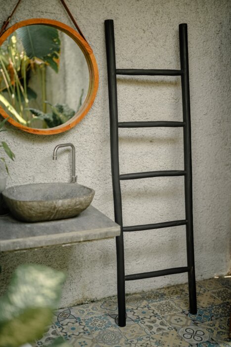 Een matzwarte houten decoratieladder, 175 cm hoog, 50 cm breed en 5 cm diep. De ladder heeft meerdere sporten met gelijkmatige tussenruimtes en staat licht hellend voor stabiliteit. De afwerking is glad en egaal, wat het minimalistische design benadrukt. 
