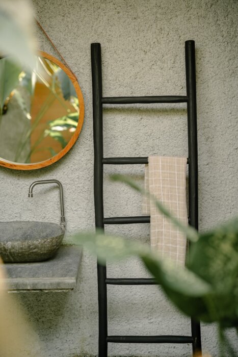 Een matzwarte houten decoratieladder, 175 cm hoog, 50 cm breed en 5 cm diep. De ladder heeft meerdere sporten met gelijkmatige tussenruimtes en staat licht hellend voor stabiliteit. De afwerking is glad en egaal, wat het minimalistische design benadrukt. 