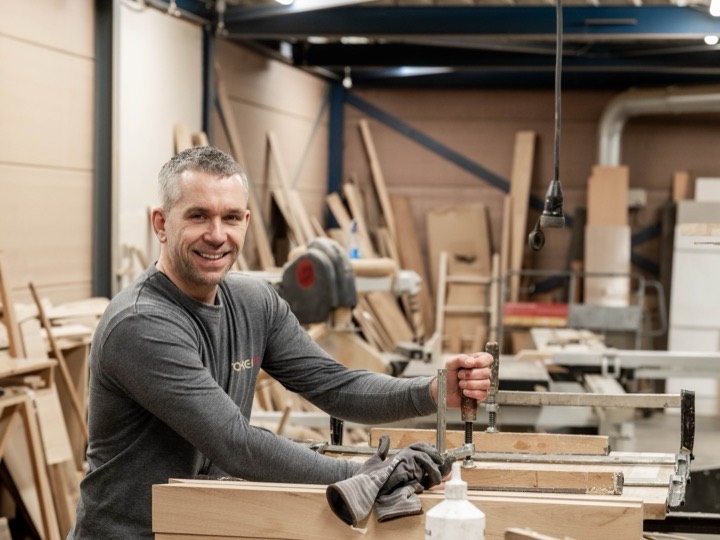 Tka home maker tolbert - Teakea Patrick de Geus, oprichter van Teakea, met lijmklemmen en een houten werkstuk in de meubelmakerij in Tolbert
